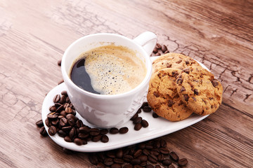 Coffee cup with chocolate cookies and coffee beans on wooden background