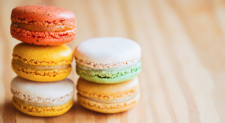 Fototapeta na wymiar Close up colorful French or Italian macaron on wood table with copy space for web banner or web cover and background or wallpaper. Macarons is French dessert served with tea or coffee.