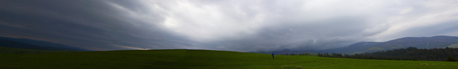 Panorama in the mountains in cloudy weather, a lonely man turned his back