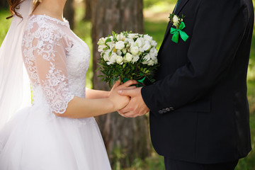 Wedding couple with bouquet of fresh flowers, bride and groom holding hands, newlyweds in love after wedding ceremony