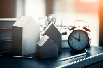 house card board model with book and alarm clock with blur background in the morning light for city...