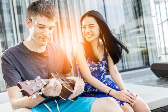 couple of caucasian and asian lover play fun with happiness and joyful and ukulele song outdoor location
