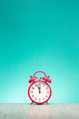 Retro alarm clock with last minutes to twelve o'clock on wooden table front gradient mint green...