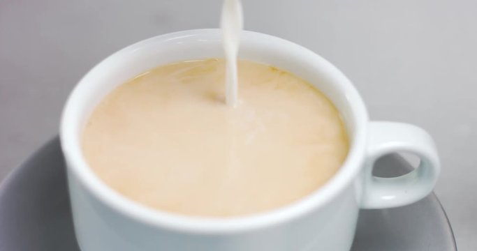 Close up video of adding milk into strong black filter coffee in a white cup with saucer