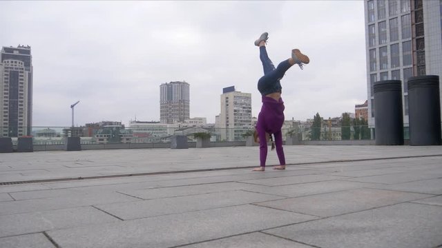 Young attractive woman doing acrobatics with cityscape on background.