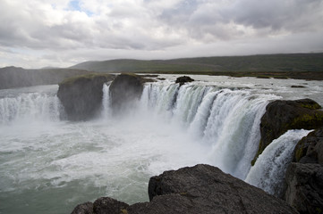 Wonderful view of Gadafoss Falls in a typical Icelandic landscape, a wild nature of rocks and shrubs, rivers and lakes.