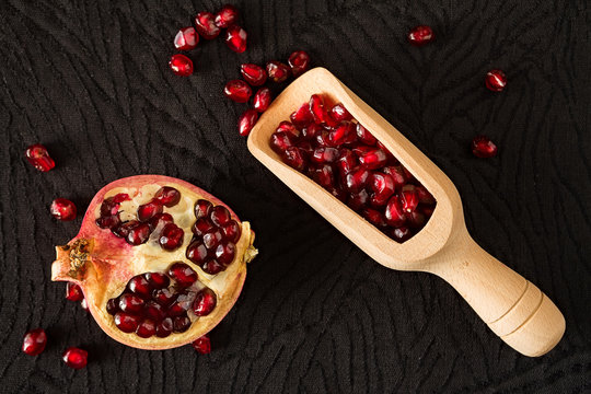 Closeup of half pomegranate fruit and bailer with seeds inside seen from above over a black textured background