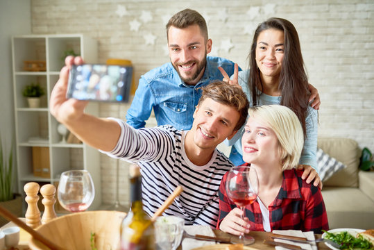 Portrait of four happy friends taking selfie at dinner table while celebrating holiday at home