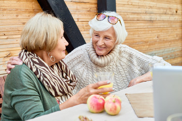 Cheerful senior women wearing knitted sweaters enjoying fresh air at lovely patio and chatting...