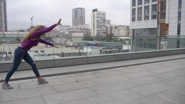 Young attractive woman doing acrobatics with cityscape on background.