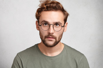 Headshot of serious stylish man with trendy hairdo looks up, has thoughtful exprression, tries to analyze all his actions, isolated over white background with copy space. People, lifestyle concept