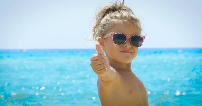 Portrait of a beautiful little girl playing in the sand on the sea, cute smiling in sunglasses, background of sea yellow sand and blue water. Concept: children, childhood, summer, freedom, kids, baby.