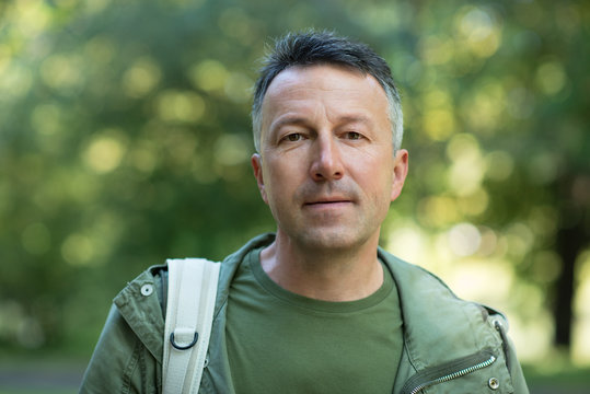 Handsome middle-aged man posing and looking at camera in autumn park over foliage. Outdoor male portrait. Male face close up.