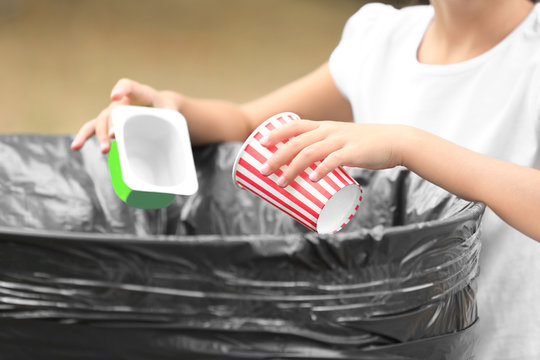 Little girl throwing garbage into litter bin outdoors, closeup
