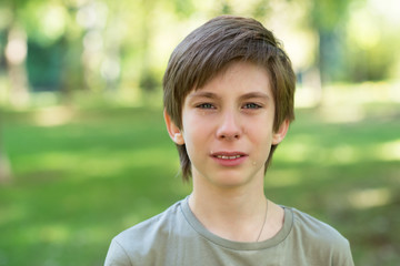 Cute handsome boy is crying outdoor. Sad early teen boy in summer park.