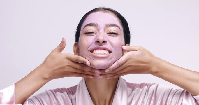 Attractive young female model removing clay cleansing peeling mask from her face on white background
