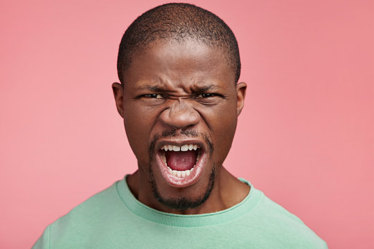 Horizontal portrait of outraged mad black young man being dissatisfied with his results and life, shouts in despair, tries to express negative emotions, being angry with people who surround him