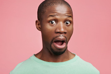 Omg. Headshot of pop eyed young dark skinned male being full of disbelief, expresses shock and frustration, keeps jaw dropped, sees something strange before him, isolated over pink background © WHstudio Leushin N