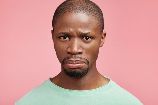 Sorrorful dark skinned male going to cry as being grieved, finds out that he has problems with health, looks in despair, isolated over pink background. Dissatisfied emotional sad African American male