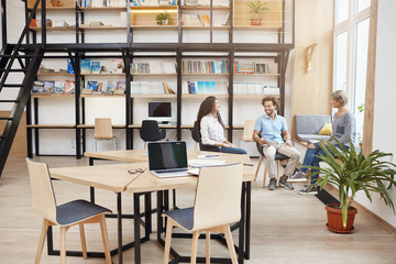 Startup, business, teamwork concept. Group of perspective young people on meeting in big modern library talking about profits of last project, looking through papers, smiling and having productive