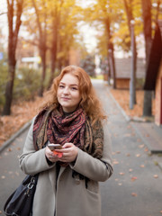 woman in coat walking in autumn Park. with phone in hand