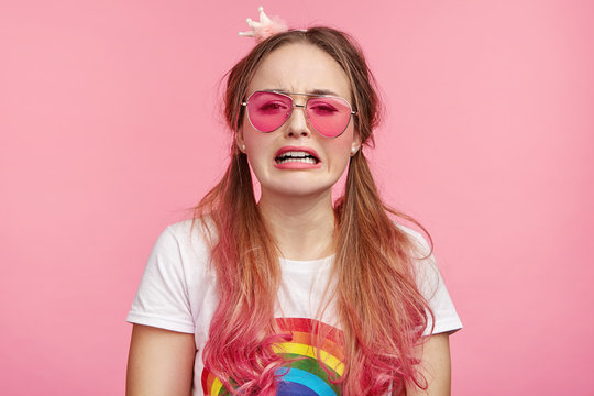 Sorrorful crying pin up girl wears pink glasses, being in despair as has no money for buying new clothes. Grieved glamour pretty woman with two pony tails has troubles in life, looks desperate
