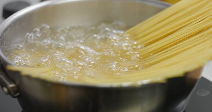 Spaghetti boiling on high heat in a large stainless steel pan, close up
