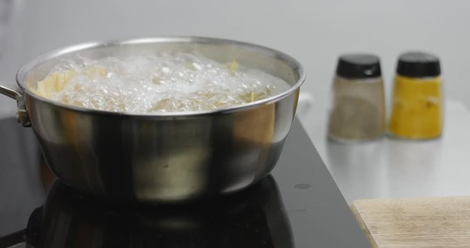 Spaghetti boiling rapidly on high heat, chef mixing with wooden spatula
