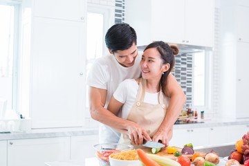 Obraz na płótnie Canvas Asian lovers or couple cooking and slicing vegetable in kitchen room. Man and woman looking each other in home. Holiday and Honeymoon concept. Valentine day and wedding theme