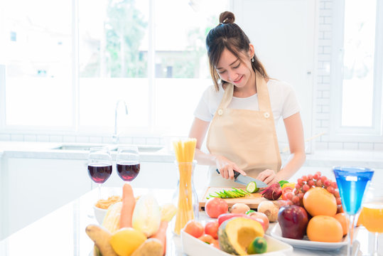 Woman Cooking And Slicing Vegetable In Kitchen Room With Full Of Food And Fruit On Table. Holiday And Happiness Concept.