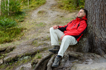 Naklejka na ściany i meble A traveler's man resting under the tree in the outdoor.A man recreates a tourist in the woods after hiking 