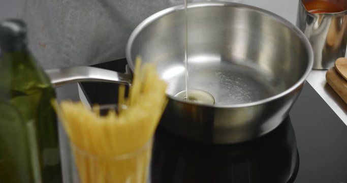 Chef pouring olive oil into a saucepan with spaghetti and tomato sauce nearby
