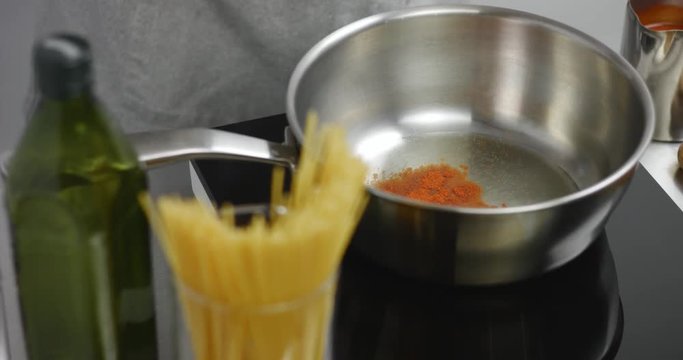 Cook adds paprika to olive oil in a stainless steel sauce pan with spaghetti in the foreground