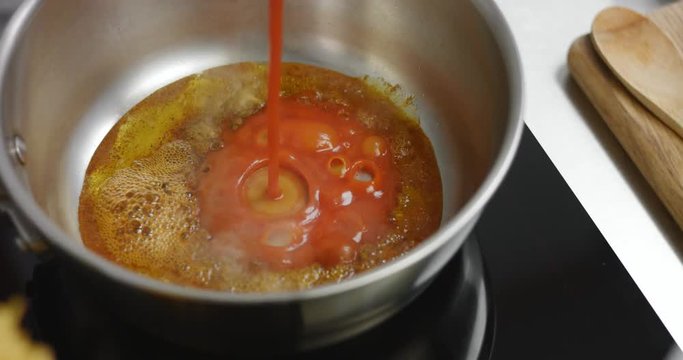 Close up of pouring thick tomato sauce into hot olive oil with paprika in a stainless steel saucepan