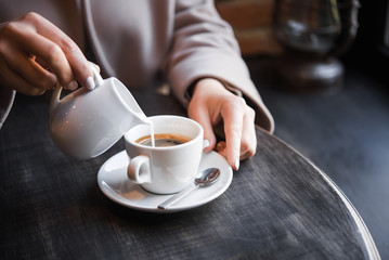 woman in a cafe pours milk cream into coffee cup