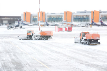 Snowplow removing snow from runways and roads in airport during snow storm, view through window