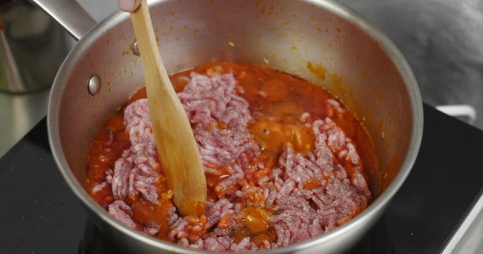 Mixing cooking bolognese sauce with a wooden spatula in a stainless steel saucepan, close up