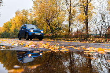 Fototapeta premium Blue car on autumn road in rainy day