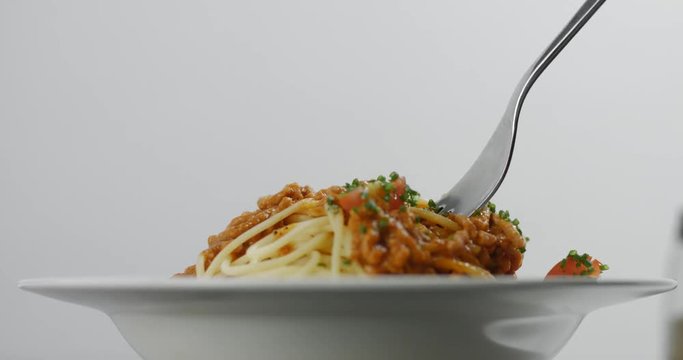 Fork twisting in succulent hot spaghetti bolognese with chives isolated on white