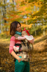 Mother carrying her baby daughter in ergonomic backpack for children