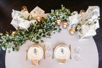 Wedding table for two decorated with white wooden candle lamps and flowers, fork and knife and glases beside plate