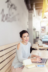 Concentrated at work woman. Confident young woman in casual wear working on laptop and mobile phone while sitting in creative office or cafe