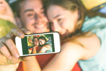 Young couple of lovers taking lying on grass taking a selfie with mobile phone - Happy teenagers in love making a self portrait using smartphone camera - Warm vintage filter -.