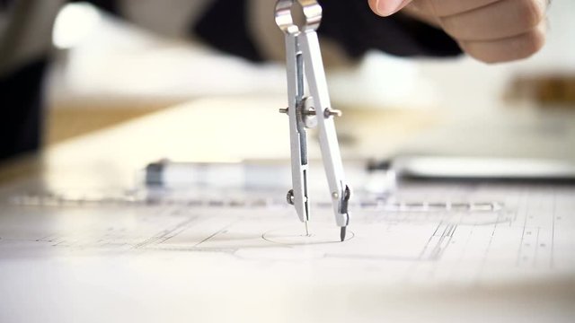 The architect draws a project of an apartment house using a pair of compasses. 4K video with shallow depth of field focus on objects.