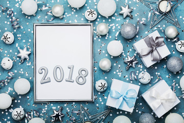 Holiday mockup or invitation. New year background. Silver frame with christmas decoration, gift box, white confetti and sequins on vintage blue table top view. Flat lay.