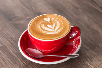 A red cup of hot latte coffee with latte art on the vintage wooden table background.
