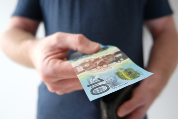 A man holding out a ten dollar Australian currency to buy, donate, share, pay someone, or invest. What does ten dollars get you?