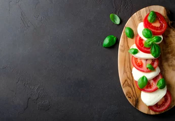  Sliced tomatoes and mozzarella on a wooden board made of olive tree, dark stone background. Top view, copyspace © losinstantes