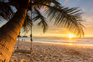 Woodden swing under coconut tree on the beach with sunset background.