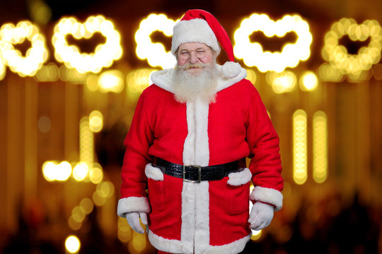 Santa Claus on blurred background. Photo of realistic Santa Claus standing on New Year lights background. Old kind Santa Claus.